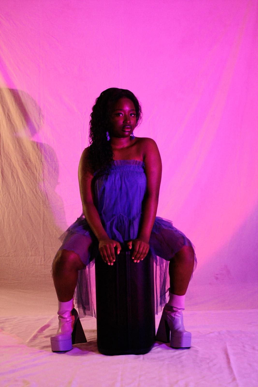 Portrait of Fatsani, seated in pink and blue studio light
